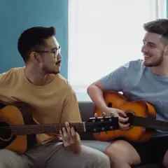 Dwóch mężczyzn gra na gitarach akustycznych. Jeden z nich ma okulary, drugi uśmiecha się.