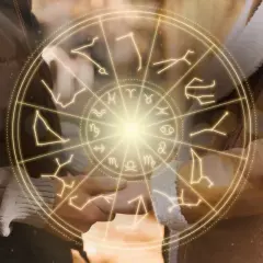 Zodiakalny krąg z symbolami gwiazd, w tym maj, otacza dłonie pary.