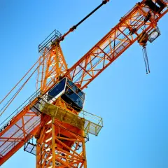 Pomarańczowy dźwig budowlany na tle błękitnego nieba. Zastanawiasz się, ile zarabia operator żurawia?