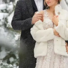 Para młoda w zimowej scenerii. Ona w białym futerku i koronkowej sukni, on w eleganckim płaszczu. Ich ślub zimą wygląda bajkowo.