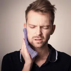 Mężczyzna z bólem policzka, przykłada zimny okład. Pewnie bolą go ósemki.