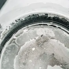 Gros plan sur le fond d'une bouilloire, montrant un tableau de dureté de l'eau avec des dépôts calcaires blancs et grisâtres.