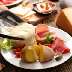 Le fromage à raclette fond sur des pommes de terre, prêt à être dégusté avec charcuterie et cornichons. Le temps de cuisson pomme de terre raclette est parfait.