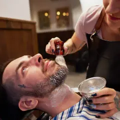 Barberka nakłada pianę do golenia na brodę klienta pędzlem.
