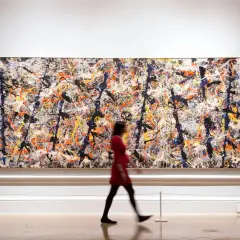 A woman in a red dress walks past a large, vibrant canvas of contemporary abstract expressionism, a masterpiece of splattered paint.