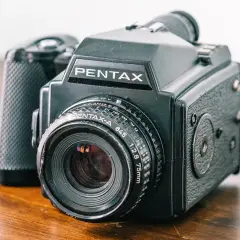 A black Pentax 645 medium format point and shoot camera with a 75mm lens sits on a wooden surface.