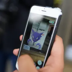Ręka trzyma smartfon, na ekranie którego widnieje fioletowy Haunter, jeden z typów pokemonów.