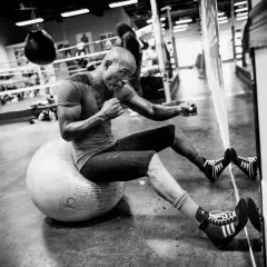 A determined Hopkins boxer, sweat glistening, trains on a stability ball in a boxing gym.