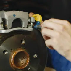 Mechanik używa klucza do odkręcenia zacisku hamulcowego, przygotowując się do wymiany tarcz hamulcowych.
