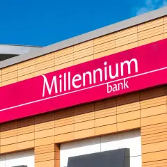 Elegancki budynek z logo Millennium bank. Jasne panele elewacyjne i fuksjowy baner z nazwą banku.