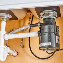 Under-sink plumbing with a garbage disposal installed, showing pipes and connections. This image illustrates how to install a garbage disposal.