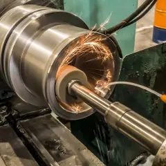 Precyzyjne szlifowanie płaszczyzn cylindrycznego elementu metalowego, iskry sypią się spod ściernicy.