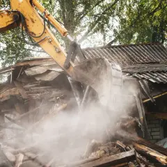 Koparka burzy stary budynek gospodarczy. Czy trzeba zgłaszać rozbiórkę budynku gospodarczego? Pył unosi się w powietrzu.