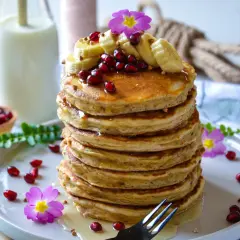 Pile de pancake banane avoine, garnie de fruits rouges, de rondelles de banane et de fleurs roses. Un délice matinal !