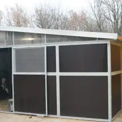 Nowa stajnia dla kucyka, z metalową konstrukcją i ciemnymi panelami. Widać kraty boksów i przezroczysty dach.