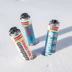 Trzy puszki pianki montażowej zimowej Soudal w śniegu. Pianka "Maxi Express" i "Classic" obok siebie, a dalej "Foam".