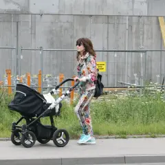 Kobieta w kolorowym dresie prowadzi czarny wózek dziecięcy.