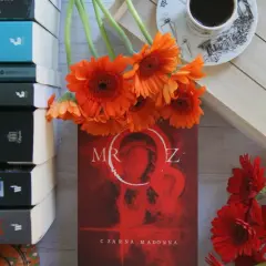 Stos książek, pomarańczowe gerbery i kubek kawy. Na okładce jednej z nich widnieje "Czarna Madonna" i tytuł "Mróz".