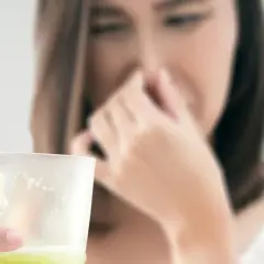 Kobieta zatyka nos, trzymając szklankę z wodą, w której wyczuwalny jest siarkowodór.