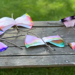 Bunte Schmetterlinge aus Kaffeefiltern, die Kinder leicht selber machen können, sitzen auf einem Holzbrett.