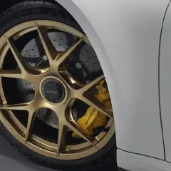 Detalle de un coche deportivo blanco con llantas doradas y pinzas amarillas. Se aprecian los discos de **frenos cerámicos** perforados, listos para la acción.