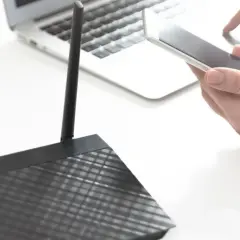 Osoba trzyma smartfon obok laptopa i routera, pokazując, jak udostępnić internet z telefonu na komputer przez USB.