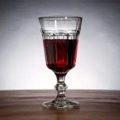 Szklanka z ciemnoczerwonym winem z jeżyn, stojąca na drewnianym blacie.