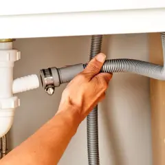 Hand connecting a dishwasher drain hose to a sink drain pipe.