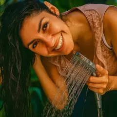 Lächelnde Frau spült sich die Haare mit Wasser. Vielleicht ein letzter Spülgang mit Apfelessig für glänzende Haare?