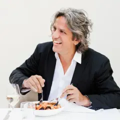 Giorgio Locatelli, chef stellato Michelin, sorride mentre gusta un piatto di pesce.