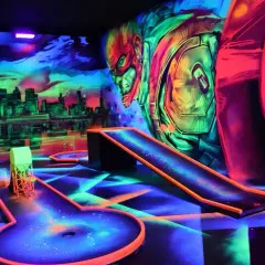 Neon-beleuchtete Bahnen und eine Skyline-Kulisse laden zum **Glow Minigolf** ein. Ein Superheld wacht über das Spiel.