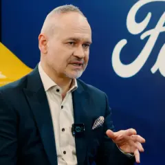 Mężczyzna w garniturze, prawdopodobnie właściciel Forda, rozmawia na tle logo marki i żółtego samochodu.