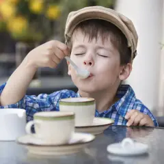 Bambino con cappellino gustando un delizioso cappuccino senza caffè, con gli occhi chiusi per il piacere.