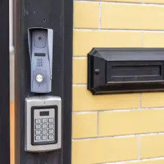 Nowy domofon z klawiaturą kodową i skrzynką na listy na żółtej ścianie bloku.