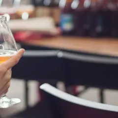 Degustacja piwa na festiwalu. Złocisty trunek w kieliszku, w tle butelki i atmosfera dobrej zabawy.