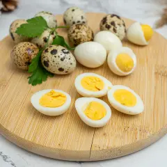 Huevos de codorniz cocidos y cortados por la mitad, mostrando sus yemas amarillas. Unos pocos huevos enteros y ramitas de perejil completan la escena.