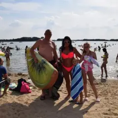Rodzina na plaży nad jeziorem Niedzięgiel, z dmuchanym arbuzem i ręcznikami, cieszy się słonecznym dniem.