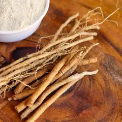 Ashwagandha-Wurzeln und Pulver auf Holz. Mögliche Ashwagandha Nebenwirkungen Haut sind selten, aber bei Einnahme zu beachten.