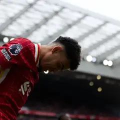 Piłkarz w czerwonej koszulce Liverpoolu z opuszczoną głową, na tle trybun stadionu.