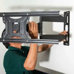 Man in green shirt mounting a TV bracket to the wall.
