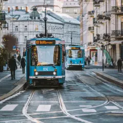 Niebieskie tramwaje na ulicy w Oslo, z budynkami po bokach.
