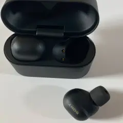 Schwarze Sony WF-1000XM6 Kopfhörer mit Ladecase. Ein Ohrhörer liegt daneben.