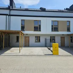 Nowoczesne domy szeregowe z drewnianymi wiatami i żółtą skrzynką gazową.
