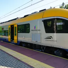 Nowoczesny pociąg Kolei Małopolskich z żółtym przodem stoi na stacji.