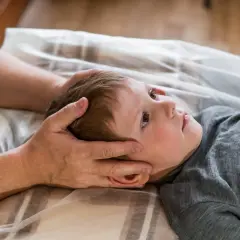 Chłopiec z obniżonym napięciem mięśniowym leży na plecach, a terapeuta delikatnie dotyka jego głowy.
