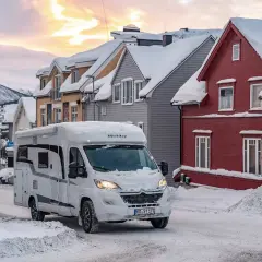 Un camping-car blanc roule dans une rue enneigée. Il semble être le camping-car le mieux isolé pour affronter le froid.