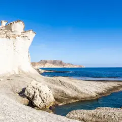 Formaciones rocosas blancas y erosionadas en una cala blanca Almería, con el mar azul intenso y montañas al fondo.