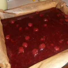 Gotowe do pieczenia ciasto bajka z wiśniami w blaszce wyłożonej papierem. Słodka, czerwona masa z całymi owocami.