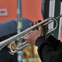 Muzyk gra na trąbce, tworząc dźwięki bluesa. W tle deszcz i ludzie z parasolami.