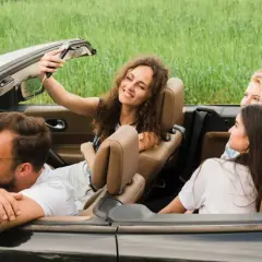 Radosne zwiedzanie Roztocza samochodem. Uśmiechnięta dziewczyna robi selfie z przyjaciółmi w kabriolecie, otoczeni zielenią.